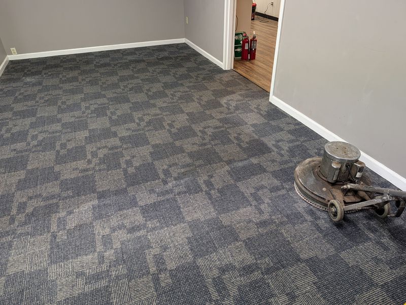 Patterned gray carpet tile in an empty room, with a floor machine in the corner